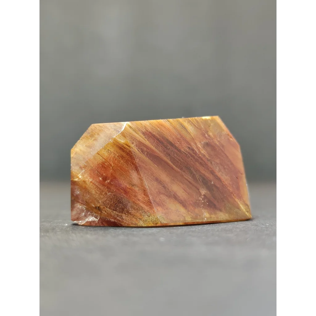 A polished translucent golden-brown amphibole angel phantom quartz polished freeform with visible internal striations