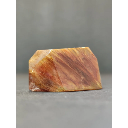 A polished translucent golden-brown amphibole angel phantom quartz polished freeform with visible internal striations