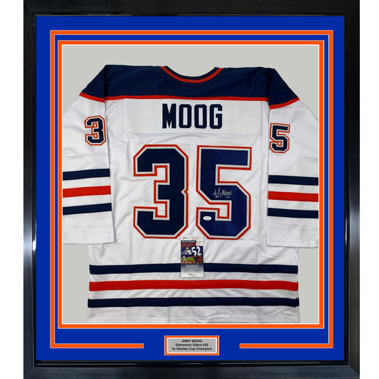 Framed white Edmonton Oilers hockey jersey number 35 with "MOOG" nameplate, navy and red stripes, signed by player, displayed against blue matting with orange border.