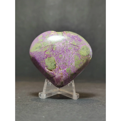 A polished heart-shaped atlantisite mineral specimen with vibrant purple and green marbled pattern on a clear stand