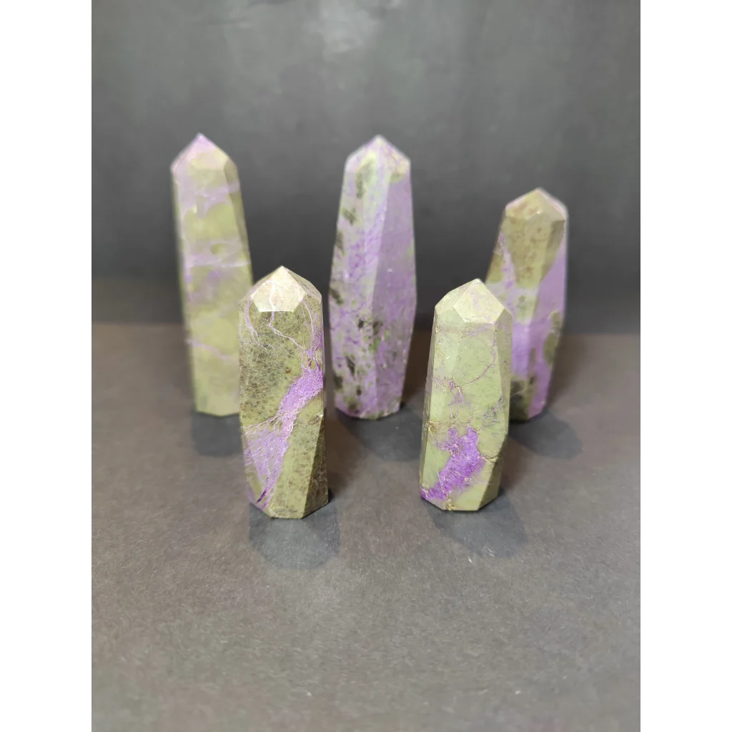 Five polished purple and green polished tower sculptures of atlantisite with faceted geometric cuts displayed upright