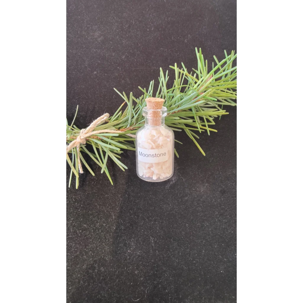 Moonstone gemstone bottle with pink chips beside pine branches