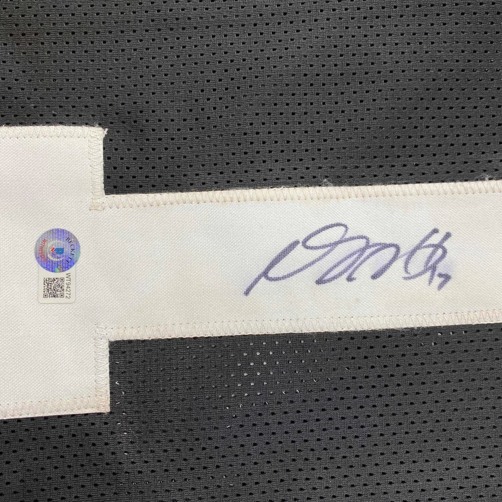 A white fabric tag with a purple ink signature and authentication sticker on a custom Davante Adams black football jersey