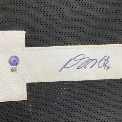 A white fabric tag with a purple ink signature and authentication sticker on a custom Davante Adams black football jersey