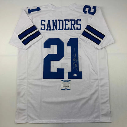 Back side of an autographed white dallas cowboys custom jersey with blue lettering and number 21 featuring sanders