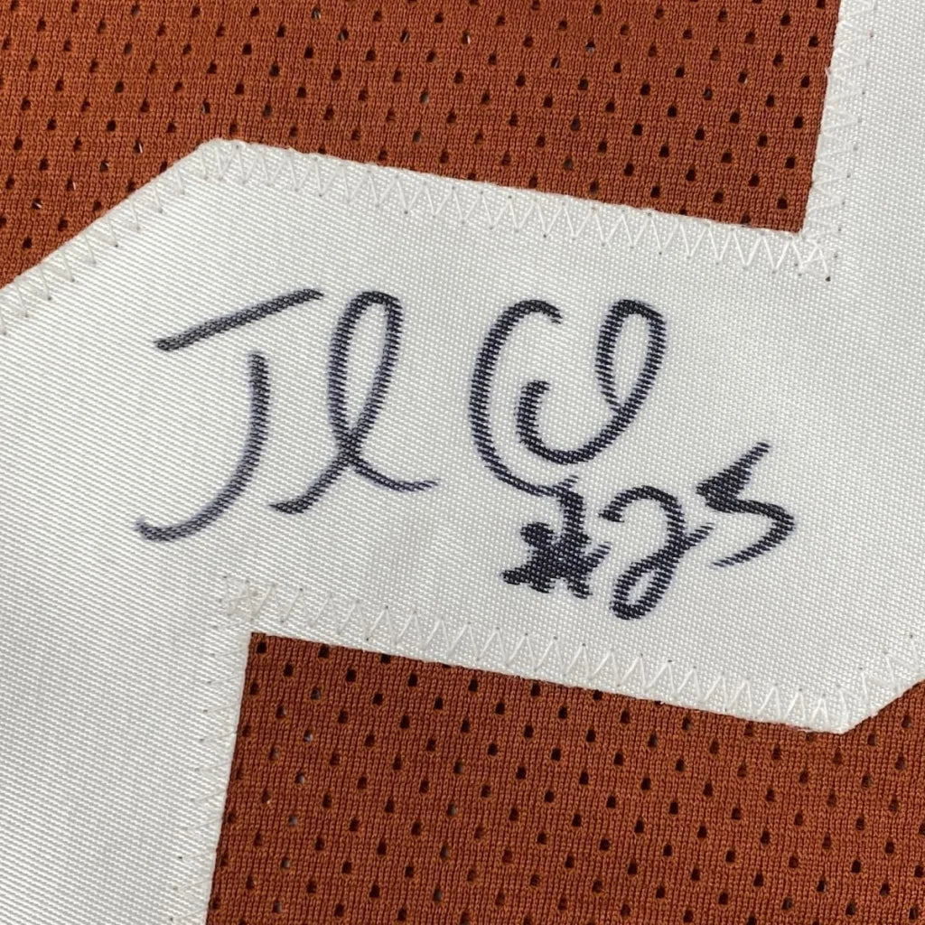 Close-up of an autographed jamaal charles texas orange custom jersey with white fabric tag and black signature on brown mesh