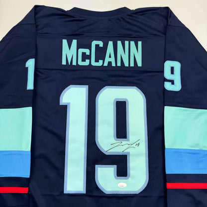 Back of a dark navy custom hockey jersey with teal accents, signed by jared mccann, number 19, from professional sports league