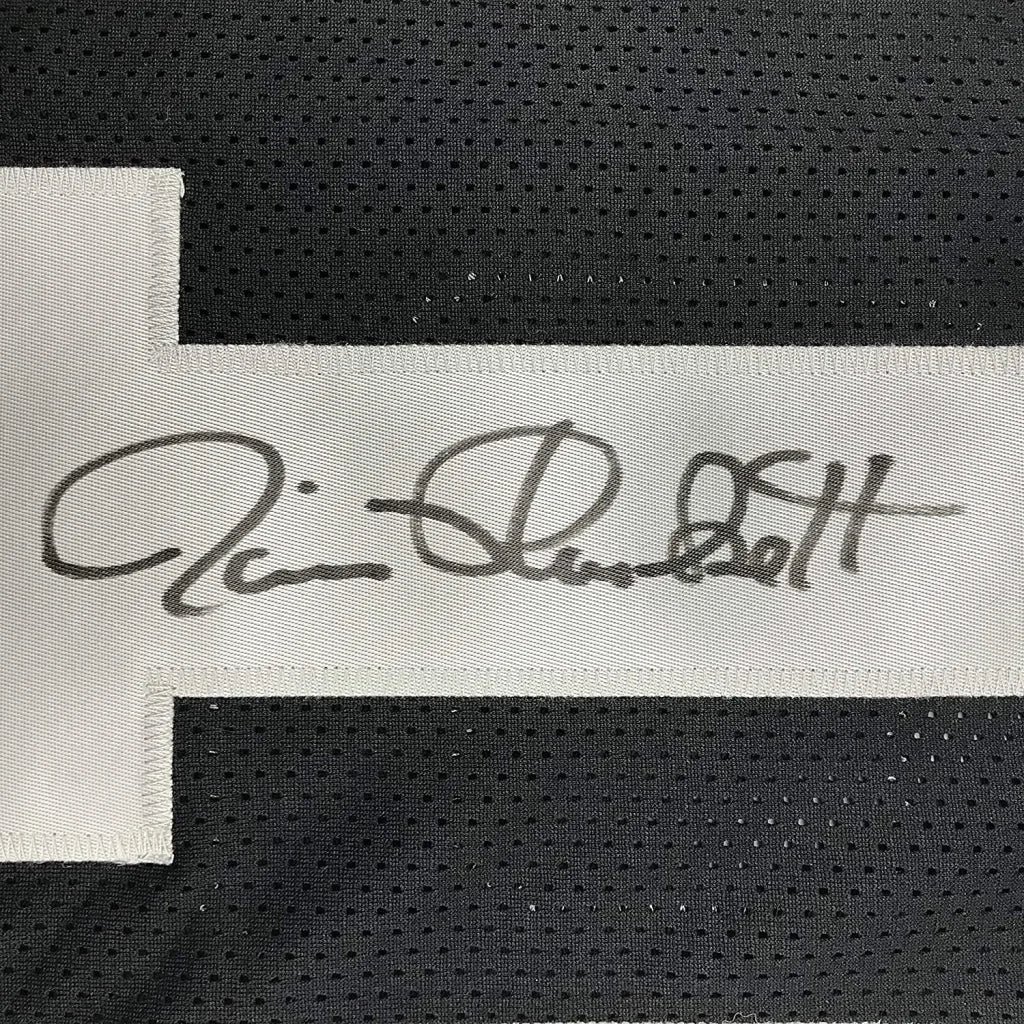 A white fabric label with a black ink signature on an autographed jim plunkett oakland black custom jersey