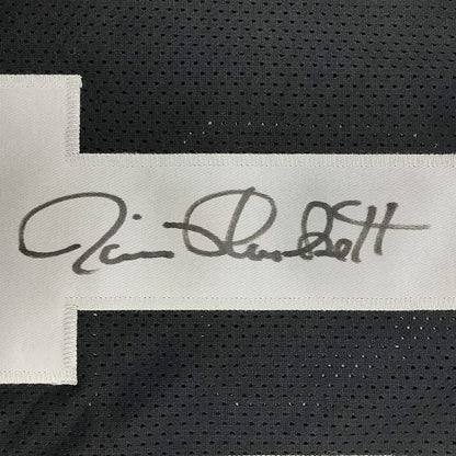 A white fabric label with a black ink signature on an autographed jim plunkett oakland black custom jersey
