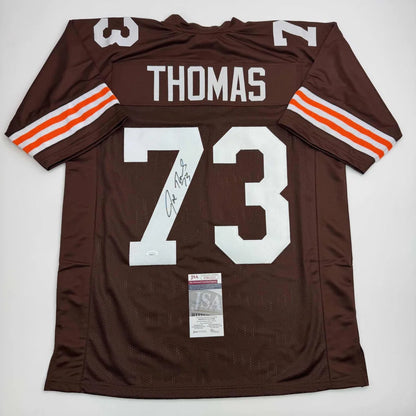 Autographed brown football jersey with white lettering orange sleeve stripes signed by joe thomas from professional sports league