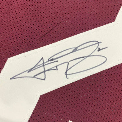 Gray ink signature on white fabric patch stitched on maroon perforated custom jersey from professional sports league