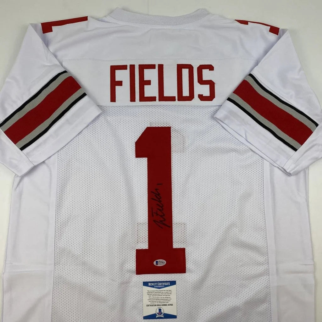 Back side of autographed white ohio state college football custom jersey with red and black striped sleeves by justin fields