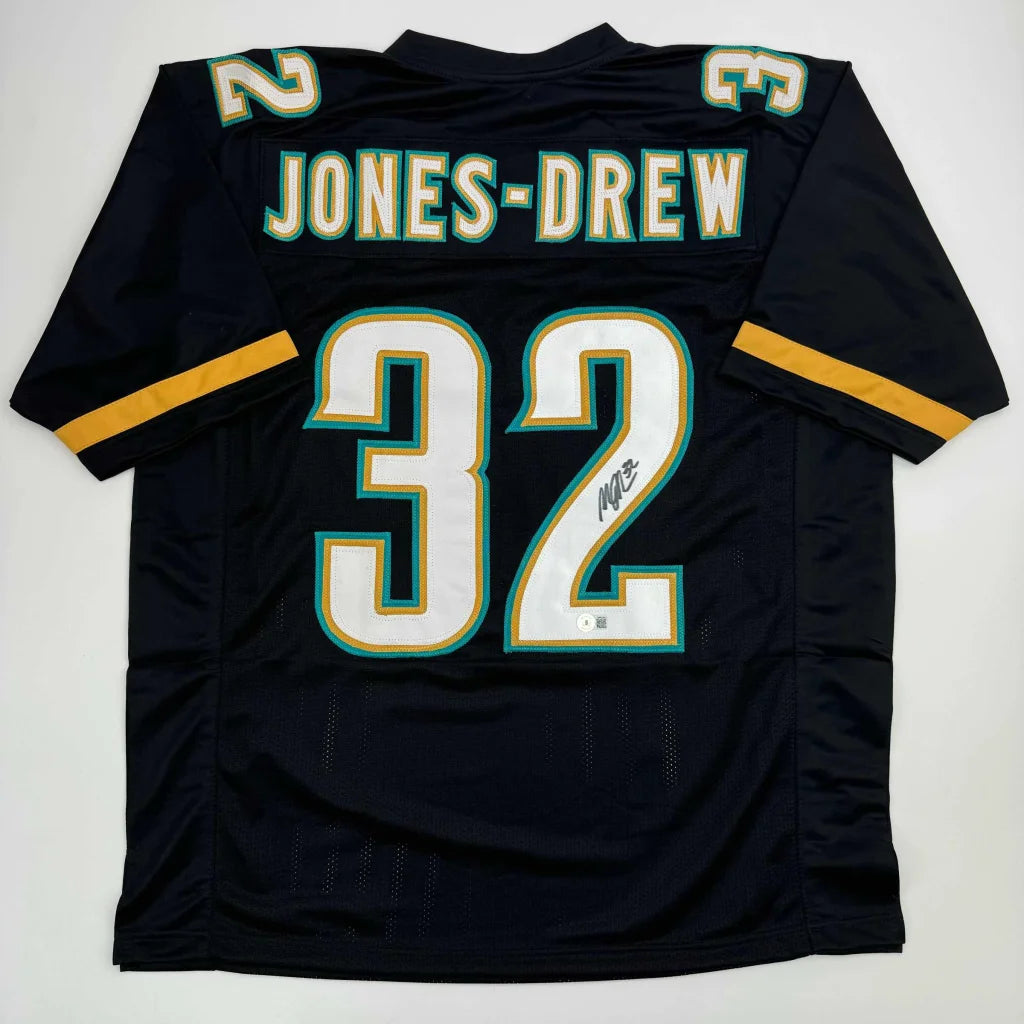 Autographed Maurice Jones-Drew custom jersey in black with white and teal lettering, number 32, gold sleeve stripes, professional sports NFL piece with Beckett BAS COA