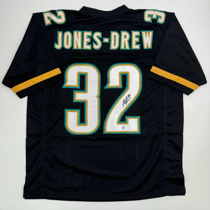 Autographed Maurice Jones-Drew custom jersey in black with white and teal lettering, number 32, gold sleeve stripes, professional sports NFL piece with Beckett BAS COA