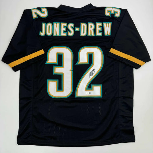 Autographed Maurice Jones-Drew custom jersey in black with white and teal lettering, number 32, gold sleeve stripes, professional sports NFL piece with Beckett BAS COA