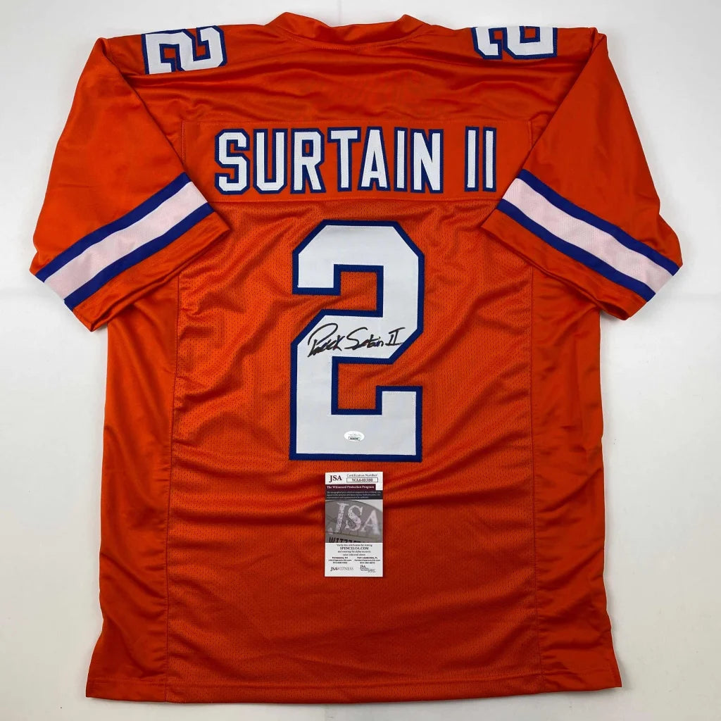 Back side of an autographed orange Denver custom jersey with white and blue lettering featuring Surtain II number 2 from professional sports league