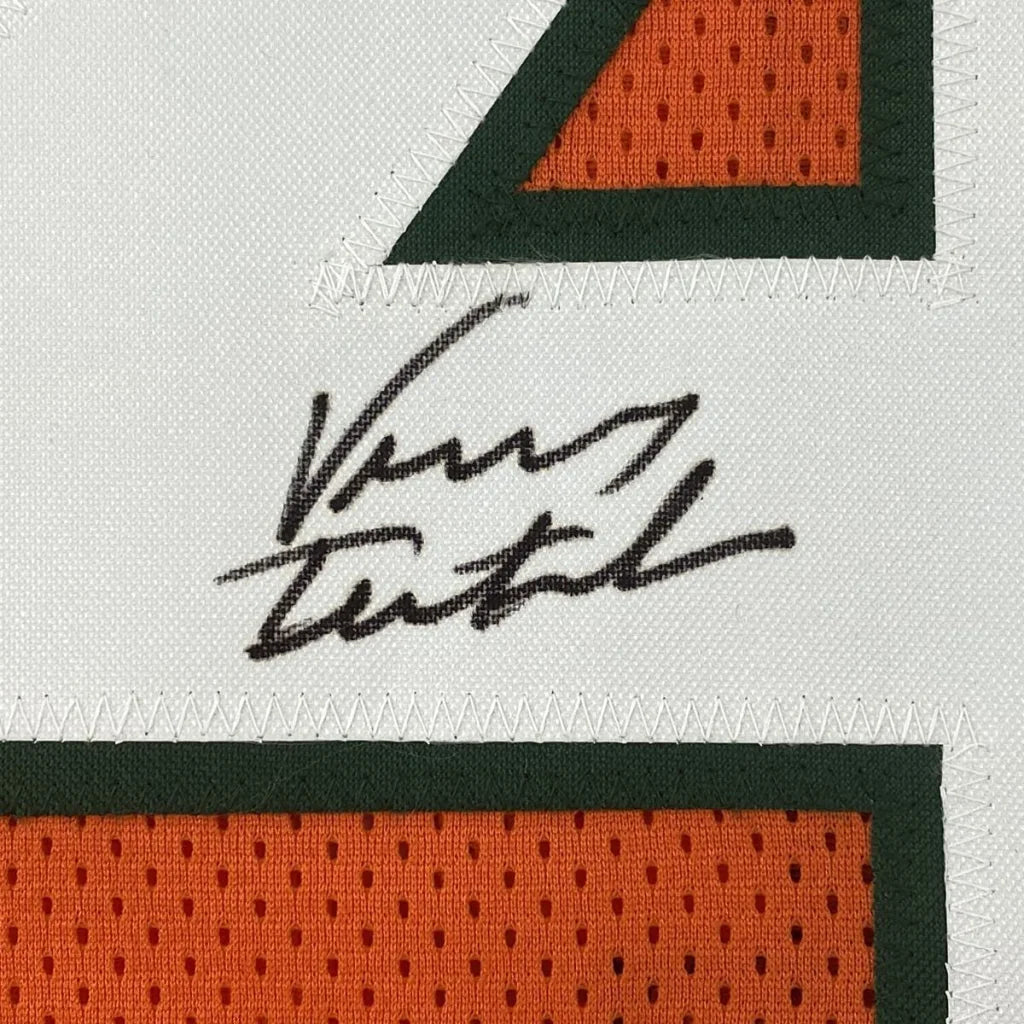 White athletic jersey with orange number outlined in dark green, signed in black ink for professional sports league fans
