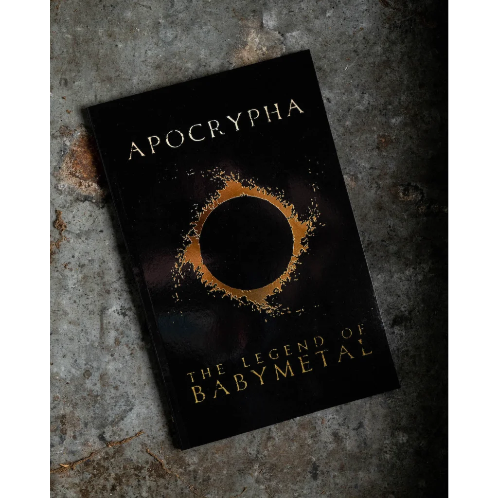 Black hardcover babymetal deluxe edition book titled apocrypha the legend of babymetal with gold foil lettering and ring design 9x15 by gmb chomichuk