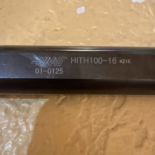 Close-up of black steel boring bar tool showing engraved text "HINAS HITH100-16 K21E 01-0125" on cylindrical shaft against tan background.