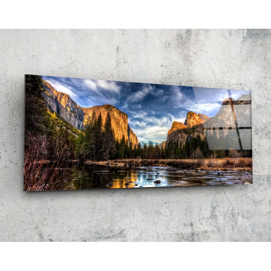 Landscape glass wall art mounted on concrete showing golden granite cliffs, river, and forested valley under blue sky.
