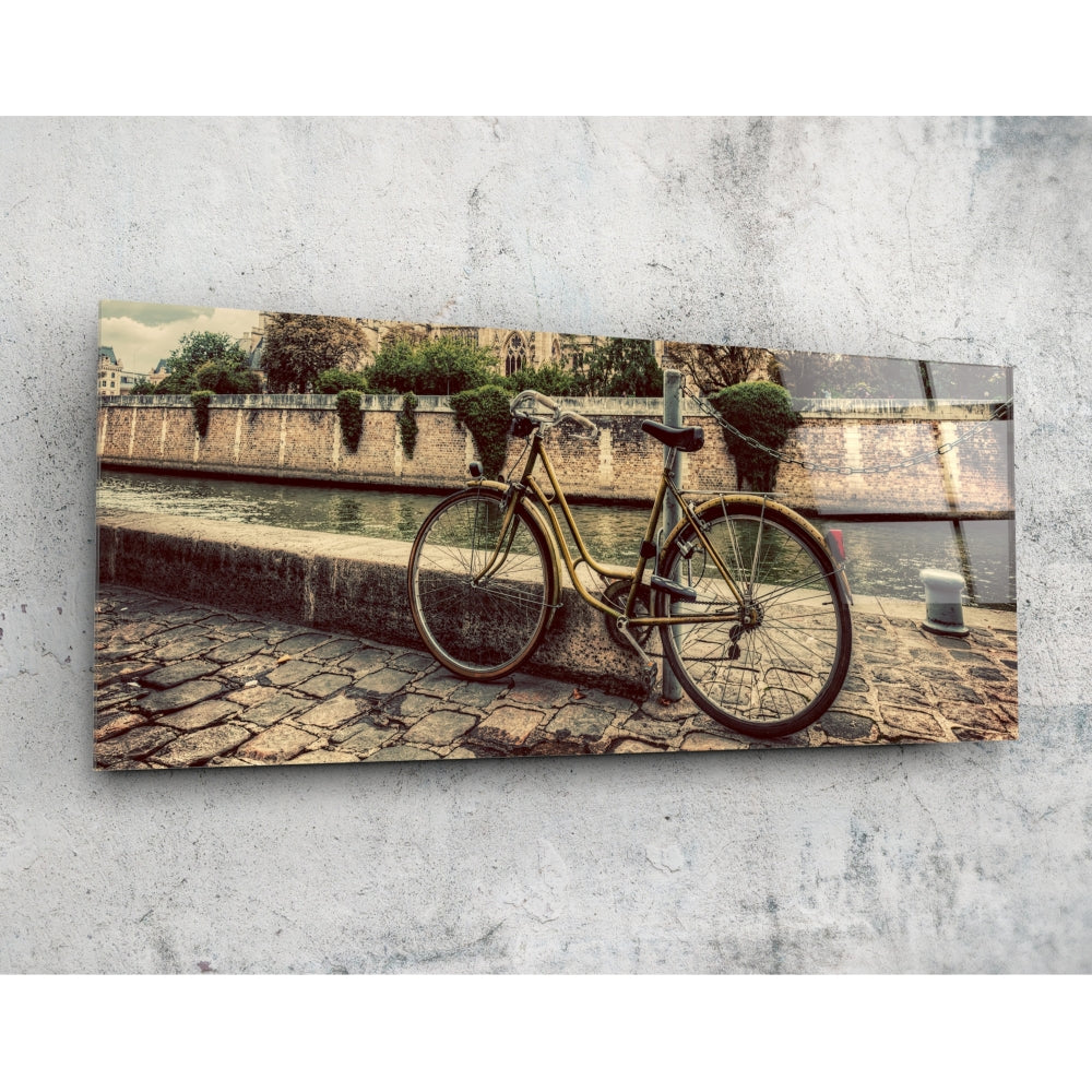 Vintage bicycle leaned against stone waterfront wall with historic buildings and bridge reflected in glass artwork.