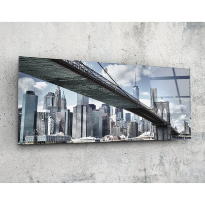 Brooklyn Bridge glass wall art mounted on concrete wall, showing Manhattan skyline and bridge underside with blue sky and clouds.