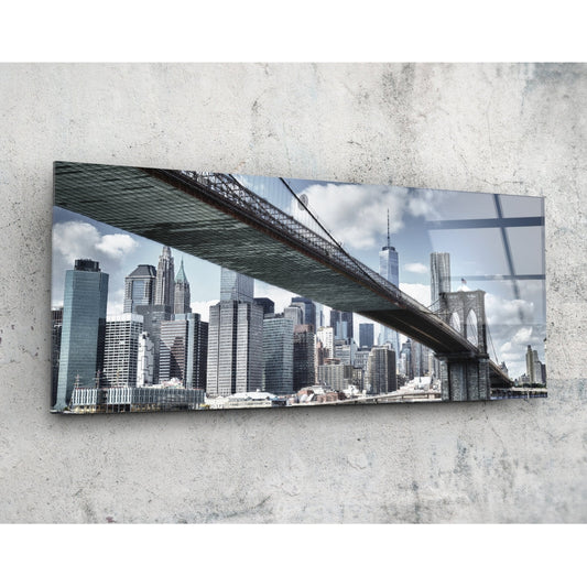 Brooklyn Bridge glass wall art mounted on concrete wall, showing Manhattan skyline and bridge underside with blue sky and clouds.
