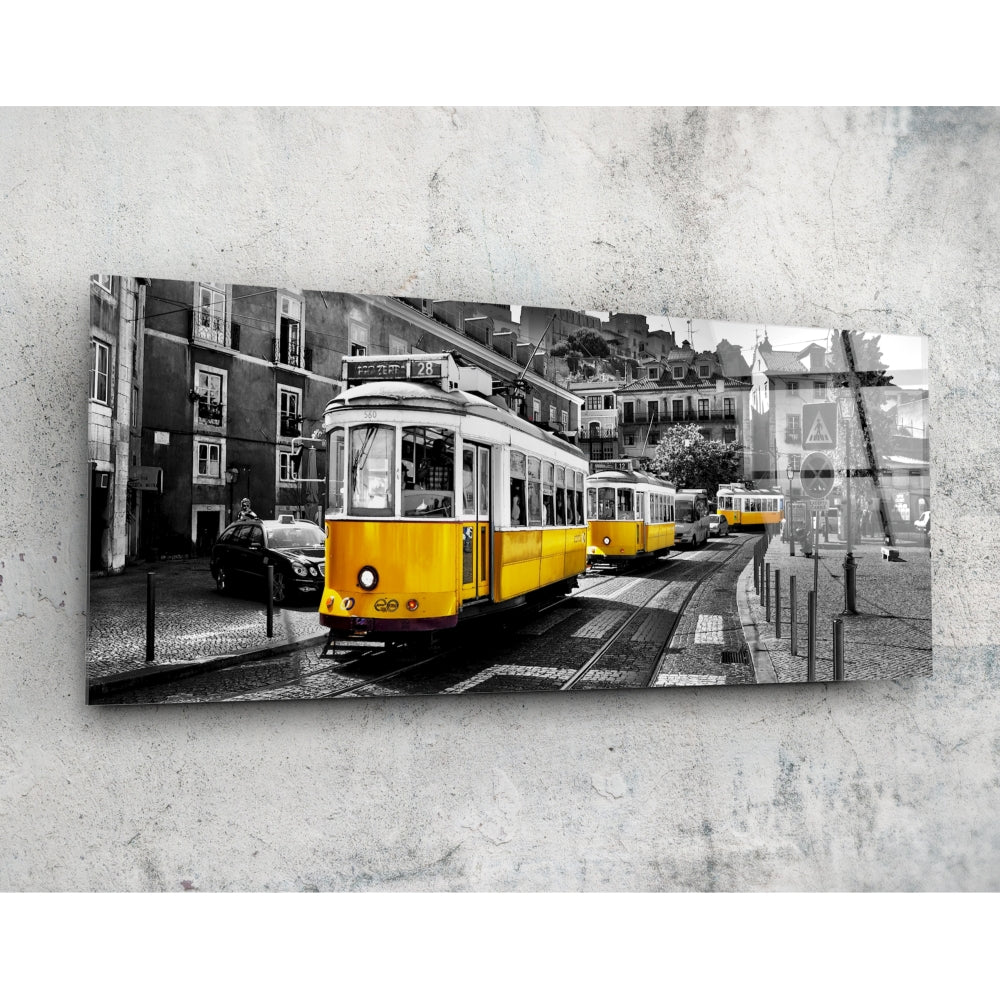 Yellow historic tram on cobblestone street with European buildings, selective color photograph mounted on concrete wall.