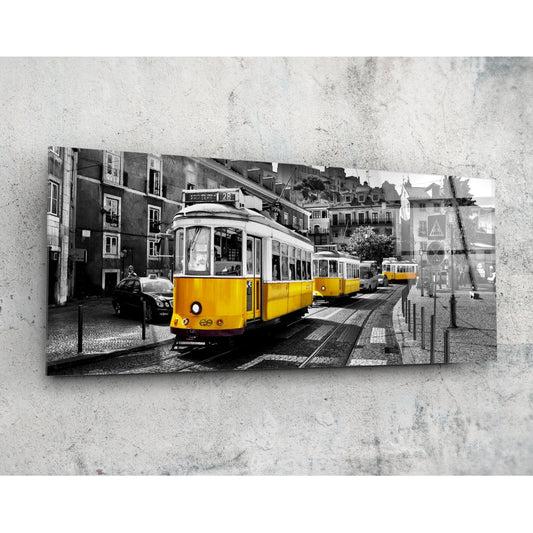 Yellow historic tram on cobblestone street with European buildings, selective color photograph mounted on concrete wall.