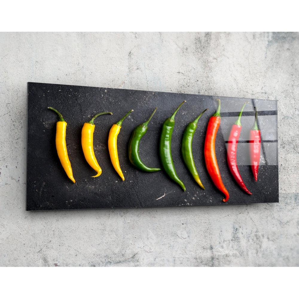 Nine fresh chili peppers arranged in color gradient from yellow to red on a black glass panel against a concrete background.