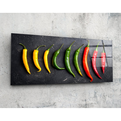 Nine fresh chili peppers arranged in color gradient from yellow to red on a black glass panel against a concrete background.