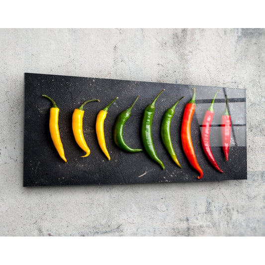 Nine fresh chili peppers arranged in color gradient from yellow to red on a black glass panel against a concrete background.