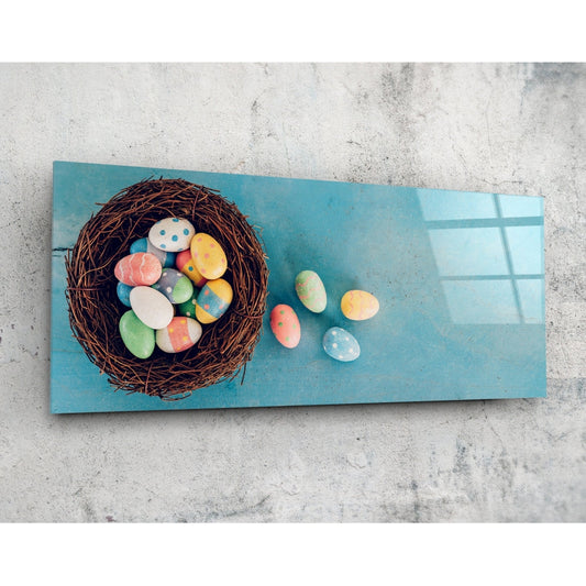 Overhead view of turquoise glass wall art displaying a woven nest filled with colorful painted eggs and scattered eggs on the surface.