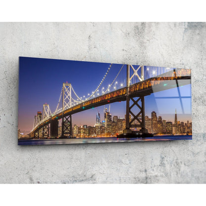 Illuminated Bay Bridge spanning San Francisco skyline at twilight, mounted on concrete wall as horizontal glass art panel.