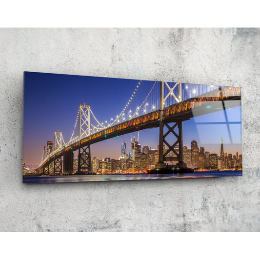 Illuminated Bay Bridge spanning San Francisco skyline at twilight, mounted on concrete wall as horizontal glass art panel.