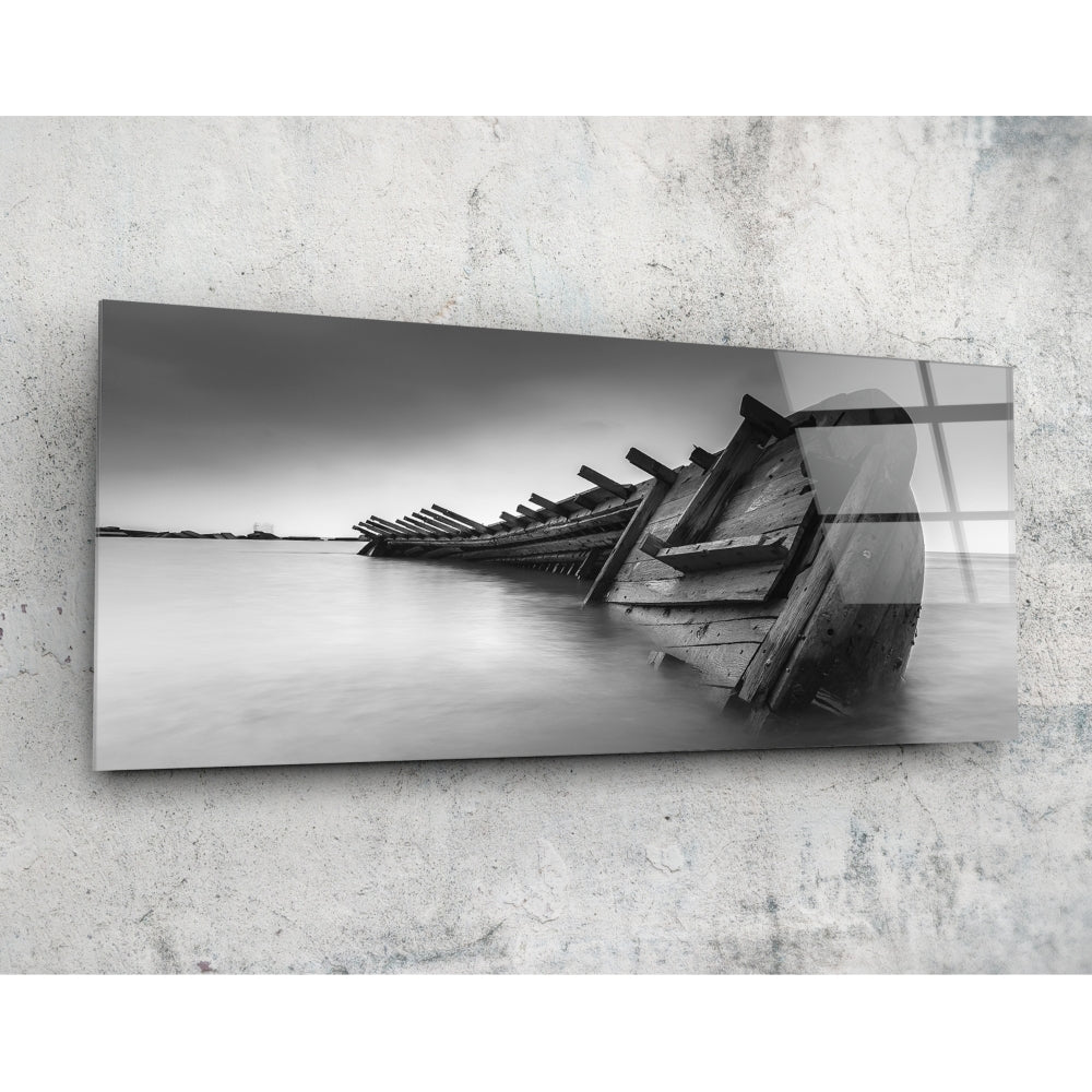 Black and white glass wall art mounted on concrete showing a shipwreck with skeletal wooden hull in shallow water.