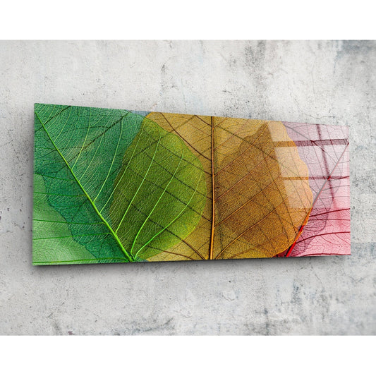 Overhead view of glass wall art displaying two translucent leaves with veining, transitioning from green through yellow to pink-red tones against concrete.