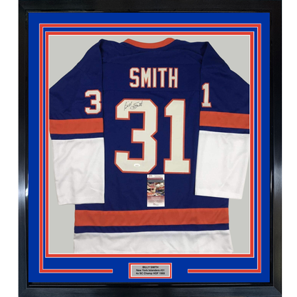 Framed navy blue New York Islanders #31 hockey jersey with red and white stripes, signed by Billy Smith, displayed against blue matting with authentication certificate visible.