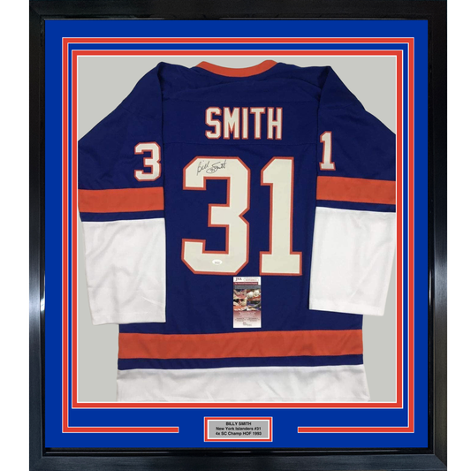 Framed navy blue New York Islanders #31 hockey jersey with red and white stripes, signed by Billy Smith, displayed against blue matting with authentication certificate visible.
