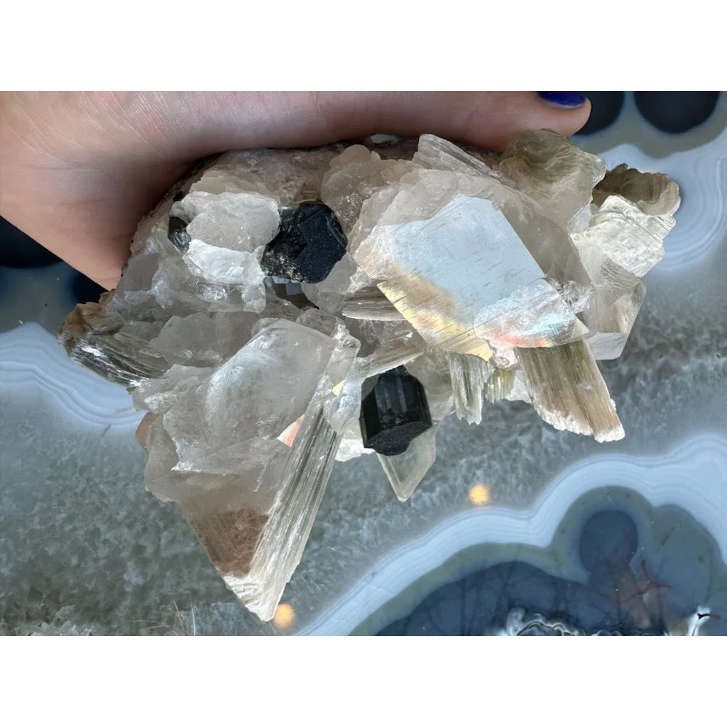 Hand holding translucent quartz with black tourmaline and blue indicolite tourmaline on matrix from Nuristan, Afghanistan