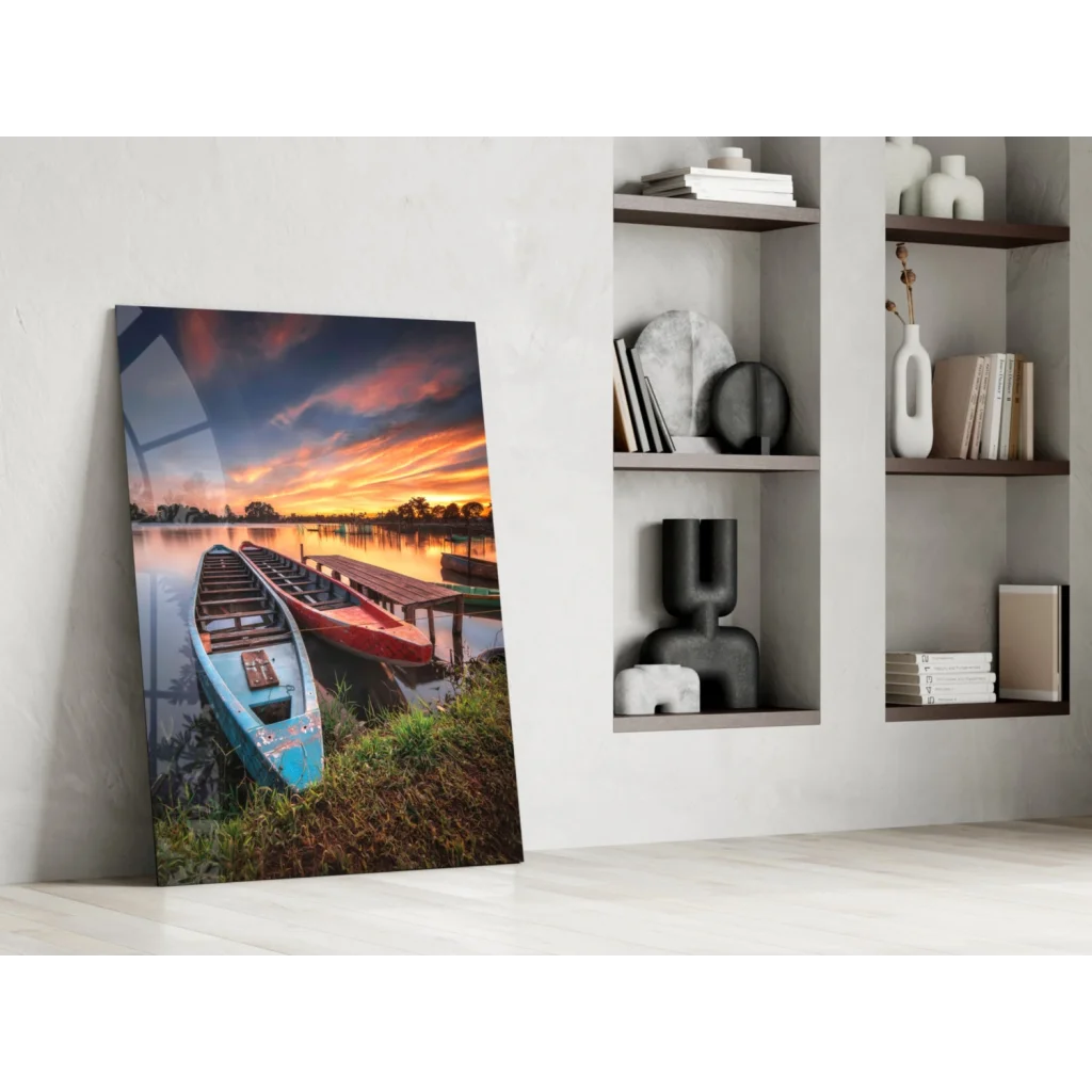 Vibrant lakeside sunset glass wall art with blue and red boats on grassy shore