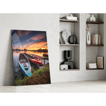 Vibrant lakeside sunset glass wall art with blue and red boats on grassy shore