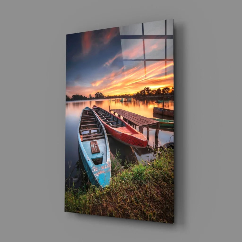 Serene lakeside sunset glass wall art with blue and red boats on dock