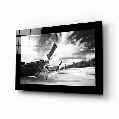 Black-and-white glass wall art of longtail boats on beach under dramatic skies