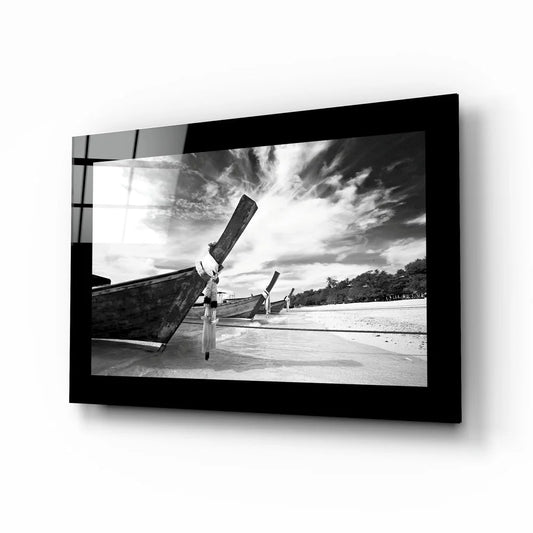 Black-and-white glass wall art of longtail boats on beach under dramatic skies
