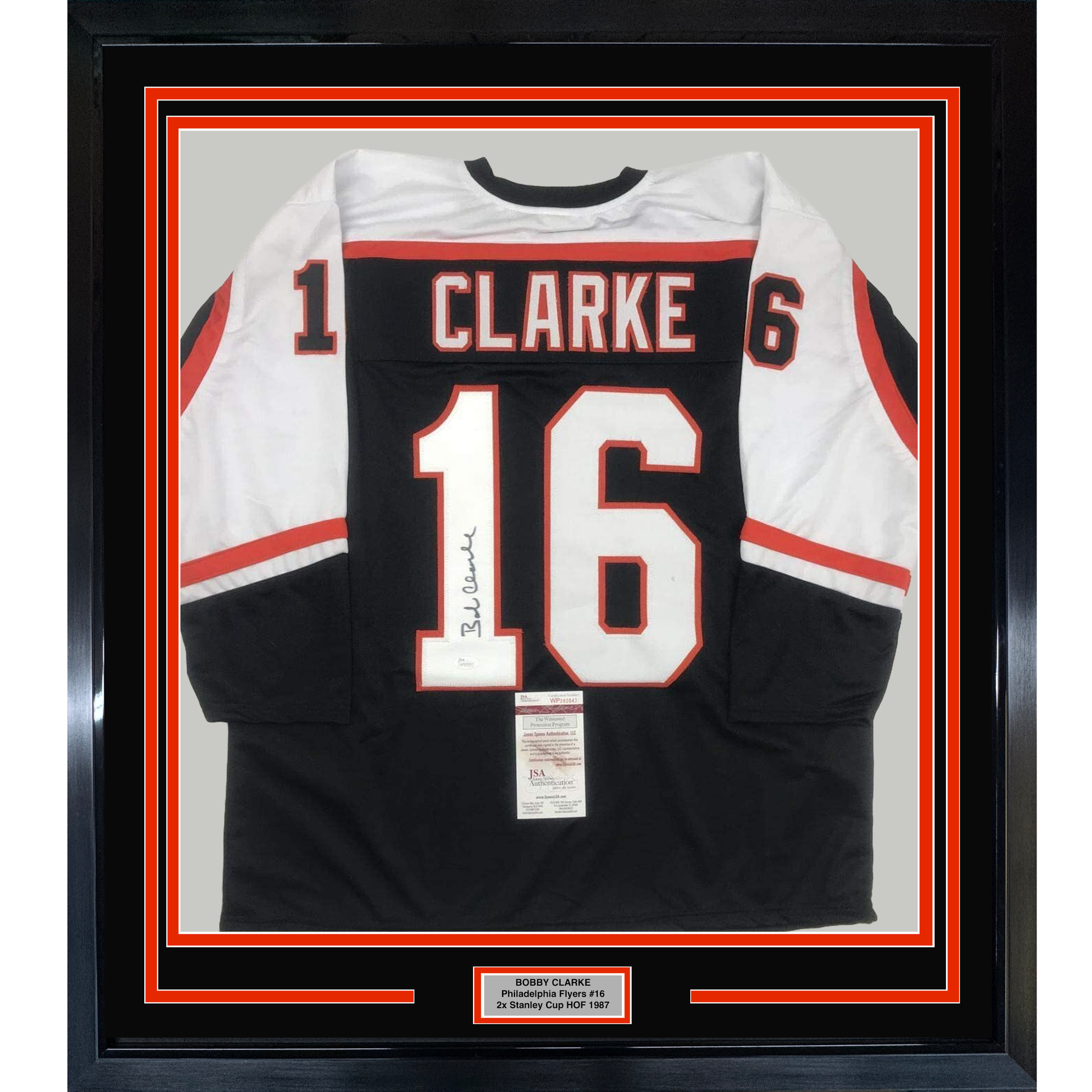 Framed black and white Philadelphia Flyers hockey jersey number 16 with "CLARKE" nameplate, signed, displayed against red and black matting with authentication certificate visible.