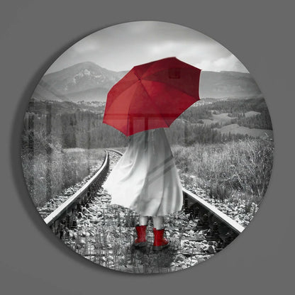Figure with bold red umbrella on train tracks, tempered glass art circle