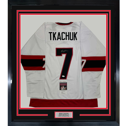 Framed white hockey jersey with red and black stripes, number 7, and "TKACHUK" nameplate, displayed flat against red and black matting with JSA certification label visible.