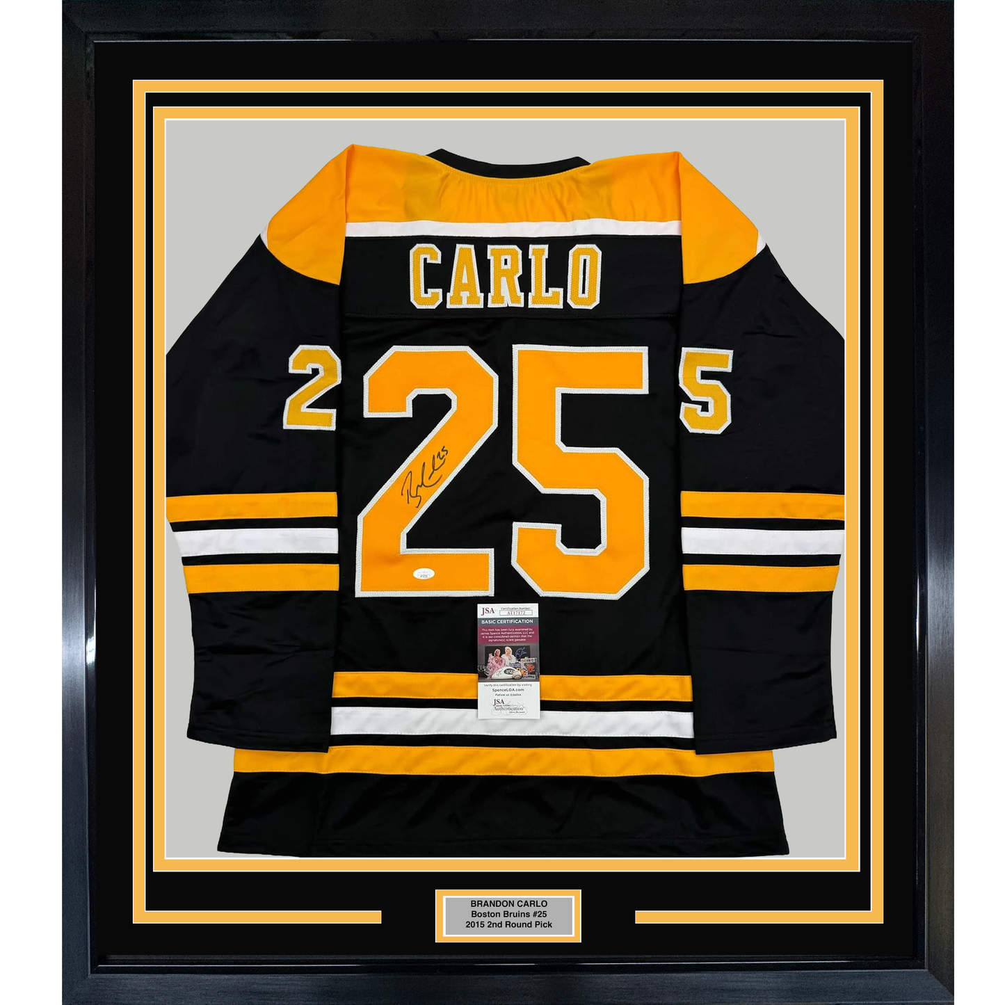 Framed black and gold Boston Bruins jersey number 25 signed by Brandon Carlo, displayed flat against light gray background with authentication certificate visible.