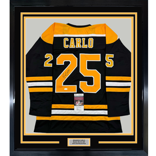Framed black and gold Boston Bruins jersey number 25 signed by Brandon Carlo, displayed flat against light gray background with authentication certificate visible.